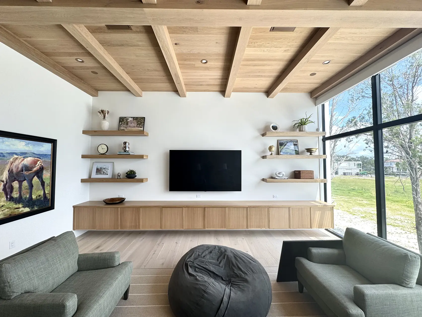 Living room with a white oak beam ceiling, floating shelves either side of the television and a full length oak credenza below