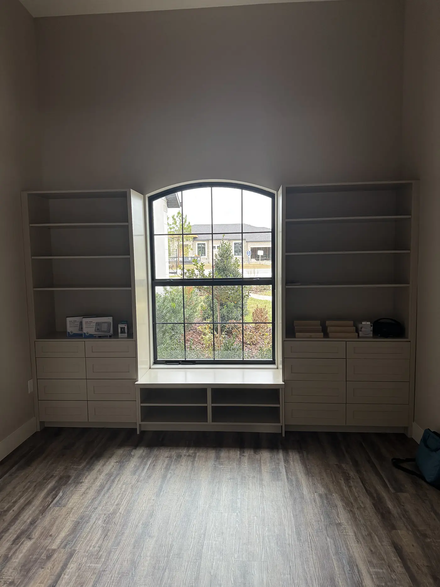 Built in shelving and drawers either side of an arched window with a bench seat between them