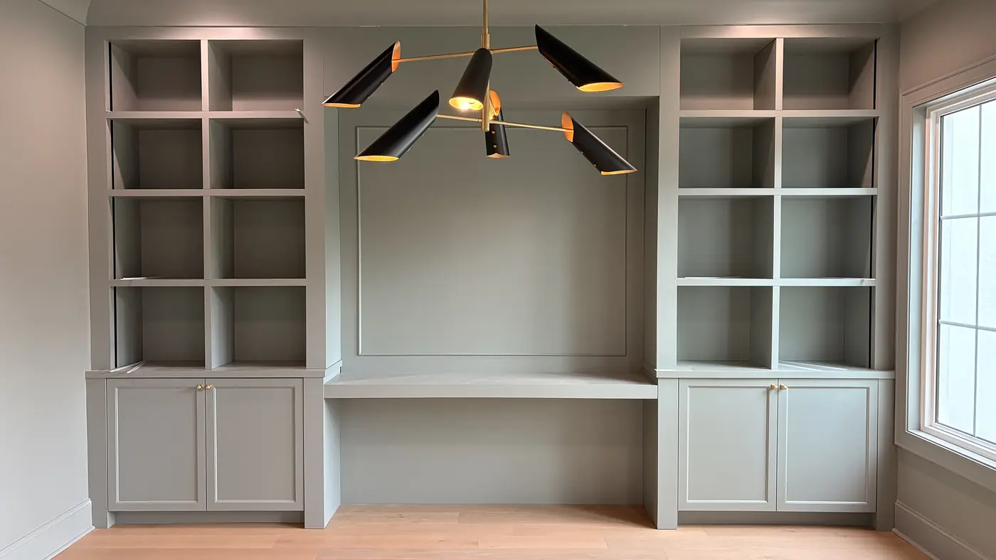 Built in desk between two shelving towers under a black and brass chandelier
