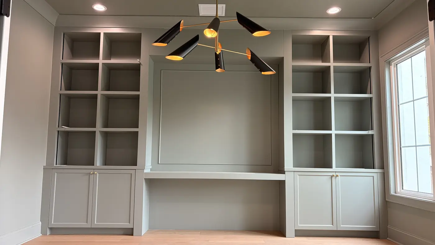 Built in desk and shelving beside a window with panelled backing behind the desk