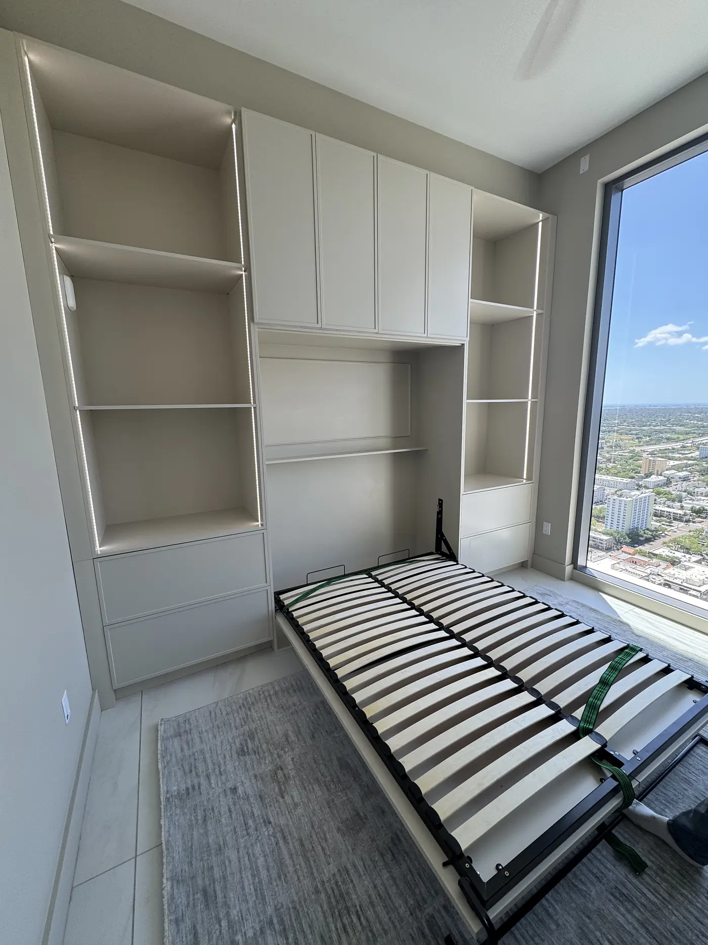 Wall bed folded down between built in shelving in a room with a city view