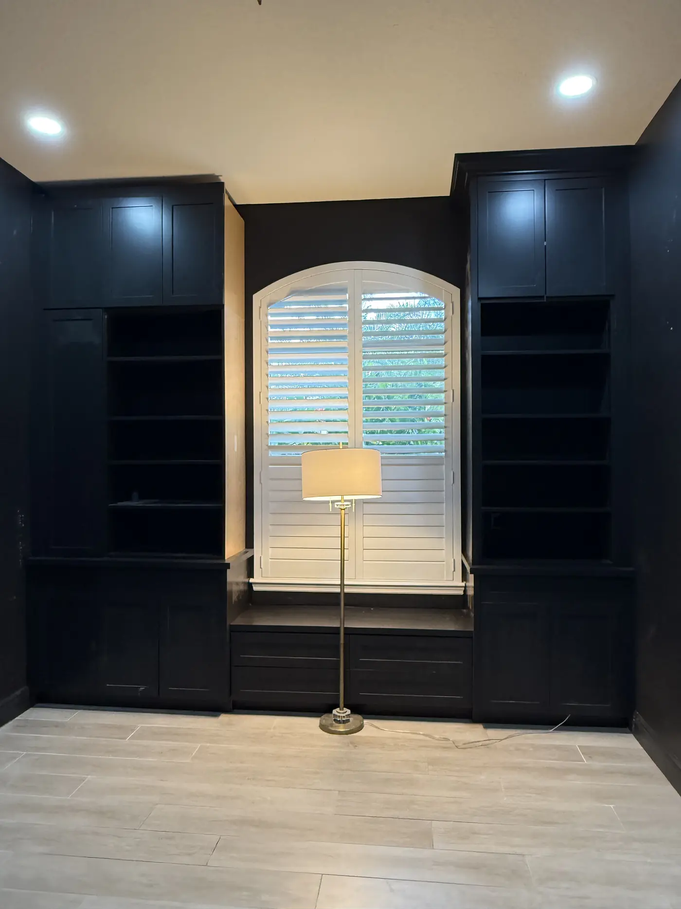 Dark navy built in bookcases either side of an arched shuttered window with a bench seat below