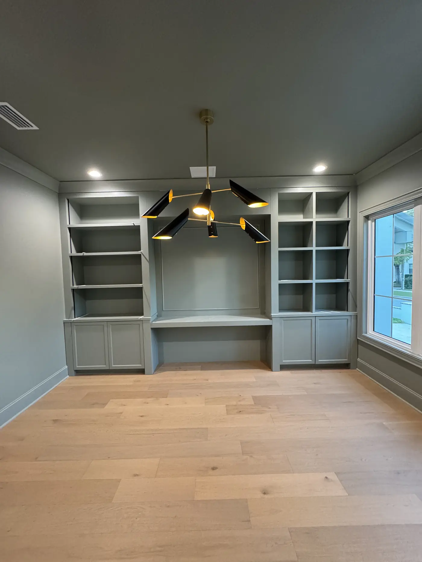 Finished sage green built in desk with cabinets and open shelving either side