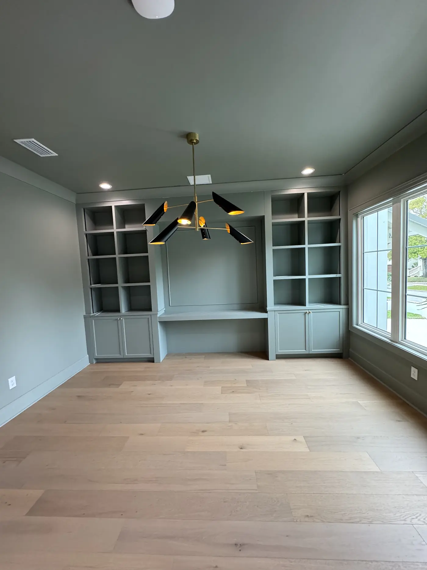 Sage green built in shelving and cabinets either side of a window