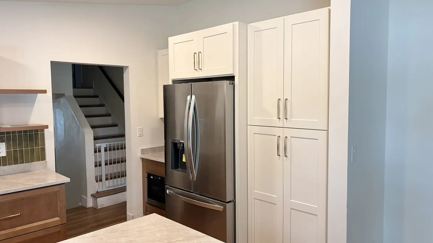 White floor to ceiling pantry cabinets beside a refrigerator at the foot of the stairs